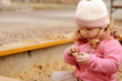 Cute toddler girl playing in sand on outdoor playground. Beautiful baby having fun on sunny warm summer day. Child with colorful sand toys. Healthy active baby outdoors plays games