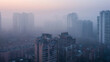 Aerial view urban cityscape with thick pm 2.5 pollution smog fog covering city high-rise buildings, orange and blue sunset sky