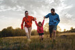 Family enjoys a playful run in the field at sunset, with a child swinging between parents, embodying the joy of active family life and the beauty of nature.