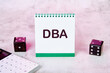 Business concept. DBA letters, DataBase Administrator or doing business as abbreviation on a white notebook near a calculator and playing dice