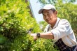 Asian gardener brings order to garden by pulling weeds spoiling picture of flowerbeds and prevent trees from growing. Asian gardener works in garden putting on gloves to protect hands from weeds