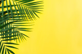 Fototapeta  - Vacation travel planning simple theme of palm leaves on uniform yellow background flat lay with copy-space