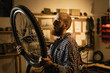 Red Haired bearded male worker holding and repairing bicycle wheel while standing in bicycle workshop.