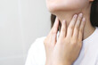 sore throat pain. Closeup of young woman sick holding her inflamed throat using hands to touch the ill neck in blue shirt on gray background. 