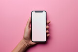 Fototapeta Konie - Woman's hand holding mobile phone with white empty screen in front of pink background with copy space.