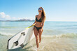  Portrait of young smiling surfer woman on the beach holding her surfboard.