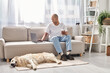 An African American man, living with myasthenia gravis, sits with his loyal Labrador dog on a cozy couch at home.