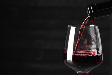 Sticker - Pouring red wine into glass against dark background, closeup. Space for text