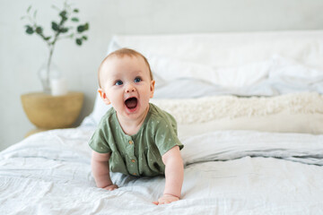 Happy baby. Cute little newborn girl with smiling face crawling on bed in bedroom. Infant baby resting playing lying down on blanket at home. Motherhood happy child childcare concept