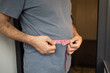 © Елена Бабанова - Overweight man measures his waist with measuring tape. Fat belly visceral fat. Body mass index, grade 1 obesity, eating disorders and physical activity, excess high-calorie food or eating disorder