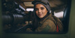 Arab woman or teenage girl is a soldier in SUV truck, wearing military uniform, motivated and ready for battle, sitting in the back seat with a device or scanner or rocket launcher, fictional location