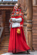 A beautiful Russian girl in red traditional Russian clothes holds bagels in her hands in the spring near a wooden house. Festive farewell to winter.
