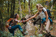 Group Of Female Friends With Backpacks Helping Each Other On Hike. People helping each other hike up a mountain at sunrise. Woman helping her friend to climb the cliff and reach the top of mountain