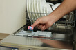© New Africa - Man putting detergent tablet into open dishwasher indoors, closeup