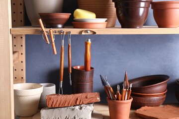 Wall Mural - Set of different crafting tools and clay dishes on wooden rack in workshop, closeup