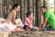 Amidst the trees, happy family shares a cozy picnic, with a child savoring a cherry as her parents relax in the peaceful forest.