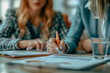 © Anek - Two women are sitting at a table, one of them writing with a pen. The other woman is looking at the writing. The scene seems to be a work meeting or a brainstorming session