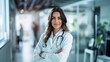 © Elena - Friendly female doctor with arms crossed in a hospital corridor
