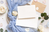 Fototapeta Boho - Cards near light blue tulle fabric knot and cream roses on plates top view copy space, wedding mockup
