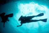 Fototapeta  - A beautiful silhouette of latina scuba divers diving underwater