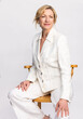 Attractive Smiling Elegant Middle Aged Woman Sitting on Stool in White Suit