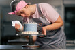 of a female baker in a professional kitchen decorating a blue cake with cream