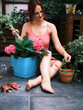 Cheerful woman in pink enjoys time gardening, surrounded by plants in various pots on her thriving balcony
