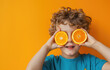 Cute boy holding orange slices over his eyes against a color background