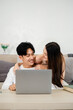 © Satori Studio - Young couple shares a playful moment with a laptop on a comfortable sofa, creating a lighthearted and loving atmosphere.