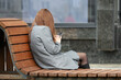 Girl in grey coat sitting with smartphone on а street bench in spring