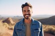 Portrait of a smiling man in his 30s sporting a rugged denim jacket over backdrop of desert dunes