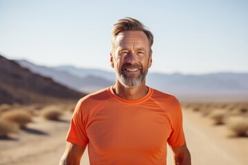 Portrait of a jovial man in his 50s wearing a moisture-wicking running shirt isolated in backdrop of desert dunes