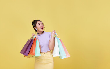 Happy pretty Asian woman carrying colorful shopping bags looking up isolated on yellow studio copy space background.