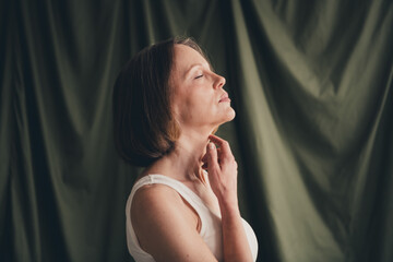 Poster - Unretouched photo of old lady touch neck skin look profile side isolated green color linen background