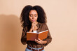 © deagreez - Portrait of intelligent minded woman with wavy hairstyle dressed brown shirt thoughtfully look at book isolated on beige color background