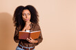 © deagreez - Portrait of puzzled woman with wavy hairstyle dressed brown shirt look at offer empty space hold book isolated on beige color background