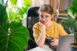 Beautiful young woman drinking coffee at work from home surrounded by indoor plants. Concept of remote work, freelancing, online learning, in the urban jungle.