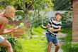 Teen boy have fun with mom at a summer garden, play water guns