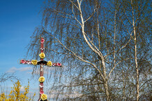 A Roadside Cross Decorated With Flowers In Spring On A Roadside Shrine Against The Background Of Birch Branches