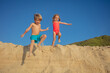 Two joyful children leap off sand dune under a clear blue sky