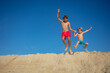 Two joyous boys leaping off sandy dune under a clear blue sky