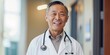 © HealthyStock - Beaming Asian male doctor in white coat outdoors with natural greenery in the background.