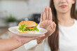 Diet, struggle asian young woman hand gesture reject to eat burger, push out or deny fast, junk food when person bring hamburger, control body overweight, eat low fat food healthy, getting weight loss