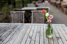 A Bouquet Of Two Pink Lisianthus, A Red Tulip And A White Rose On A Wooden Table In A Glass Vase In A Street Cafe.