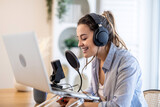Fototapeta  - Woman wearing headphones sitting at a desk speaking into microphone and recording a podcast
