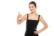 Young woman wearing black dress over white studio background approving doing positive gesture with hand, thumbs up smiling and happy for success. Winner gesture