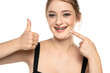 Cheerful happy young woman with blonde hair gesturing thumb up while pointing finger at braces on her teeth isolated over white background. The concept of a healthy snow-white smile. Daily dental care