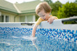 Cute funny toddler boy having fun by an outdoor pool. Kid playing with water. Family fun in a pool. Summer activities for the entire family.
