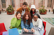 © Jose Calsina - A diverse group of cheerful teenage students is huddled together in the university campus, diligently working on a assignment using their laptop, focused on gathering information from the computer