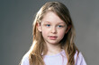 Portrait of  little girl with long blonde hair and blue eyes, looking to the side, gray background